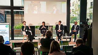 Die Expert*innen des KEI Podiums diskutieren über industrielle Flexibilisierungspotenziale. Bild v.l.n.r.: Katrin Düning (Senior Advisor Bundespolitik, TenneT), Moderatorin Hanna Gersmann, Prof. Dr. Alexander Sauer (Fraunhofer-Institut für Produktionstechnik und Automatisierung IPA) und Jean Théo Ghenda (EUROFER, Brüssel). Digital zugeschaltet: Dr. Habibullah Qureischie | Beisitzer in der Beschlusskammer 4, Bundesnetzagentur (BNetzA) und Eric Lecomte von der Generaldirektion Energie der Europäischen Kommission.