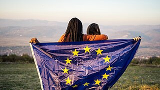 Zwei Jugendliche vor einem Bergpanorama halten eine EU-Flagge