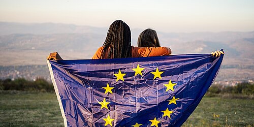 Zwei Jugendliche vor einem Bergpanorama halten eine EU-Flagge